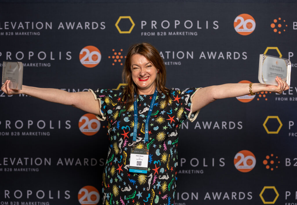 Claire Mason, Founder and CEO of Man Bites Dog holding two gold awards at the US B2B Marketing Elevation awards